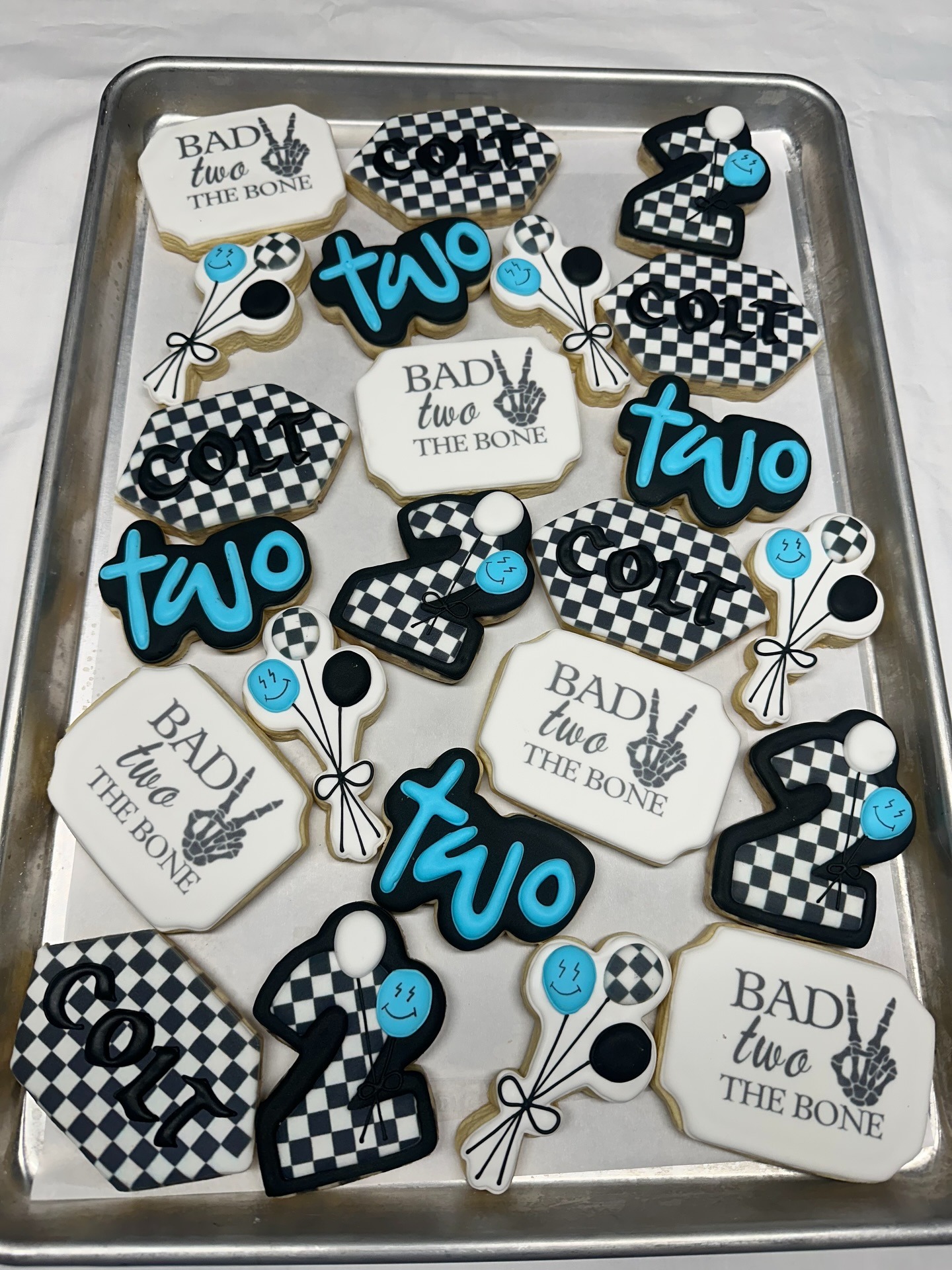 Bad Two The Bone 2nd birthday cookies — checkered black-and-white, bright blue 'two' lettering, balloon and skeleton-hand details on a sheet pan